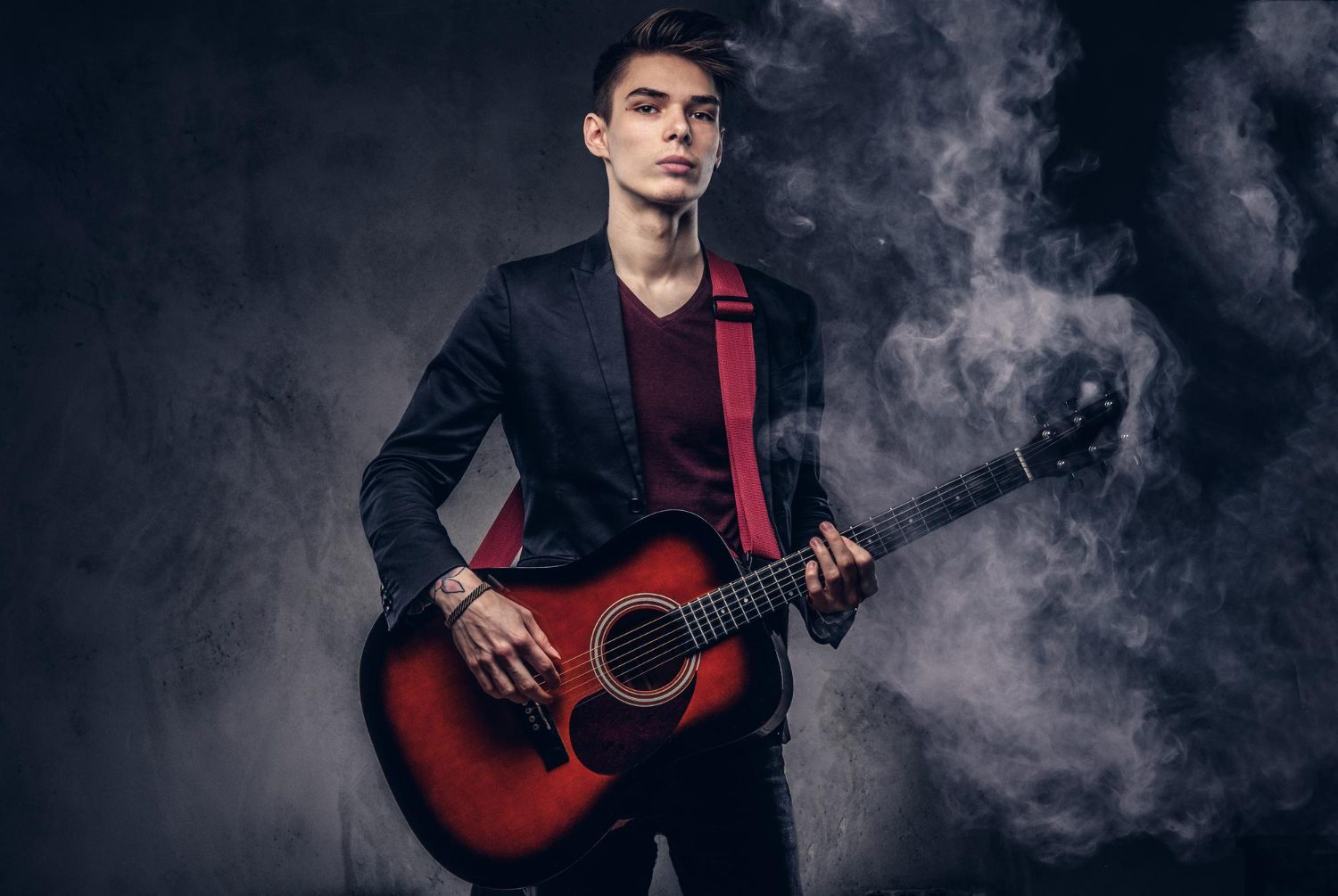 stylish-young-musician-with-stylish-hair-elegant-clothes-with-guitar-his-hands-playing-posing-dark-background